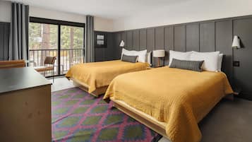 A hotel room with two beds, a desk, a chair, and a balcony with a view of trees.