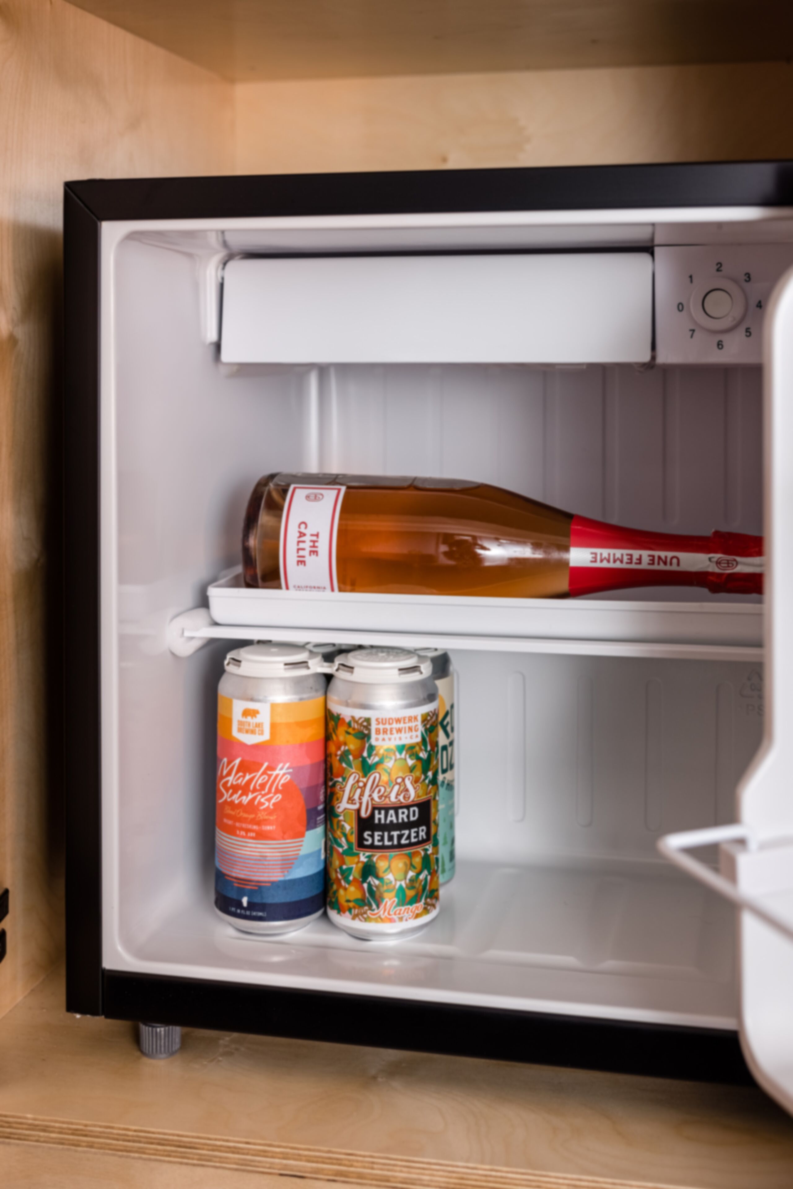 A refrigerator with a bottle of wine and two cans of beer.