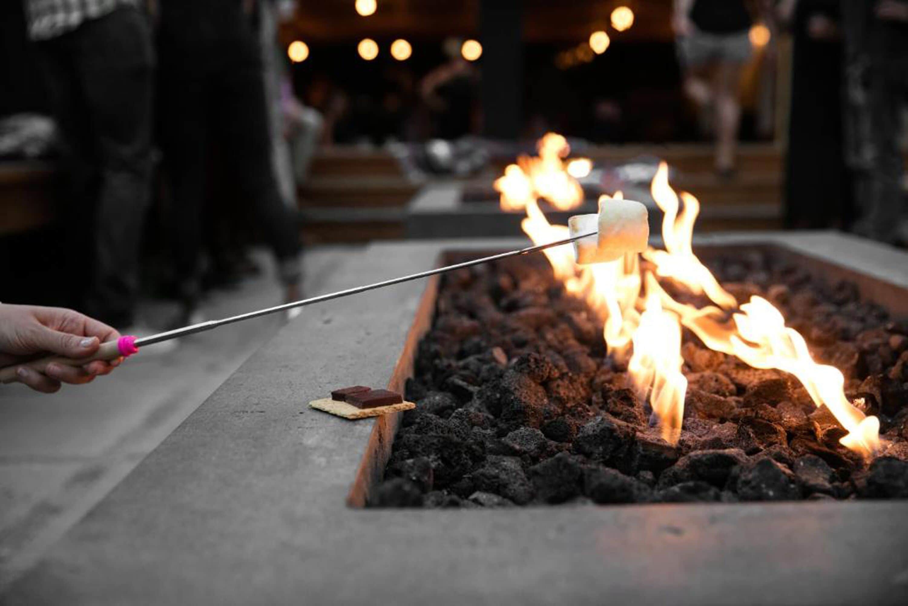 A person holding a stick with a marshmallow over a fire pit.