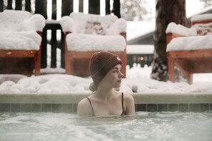 Una persona en un jacuzzi con bancos cubiertos de nieve al fondo.