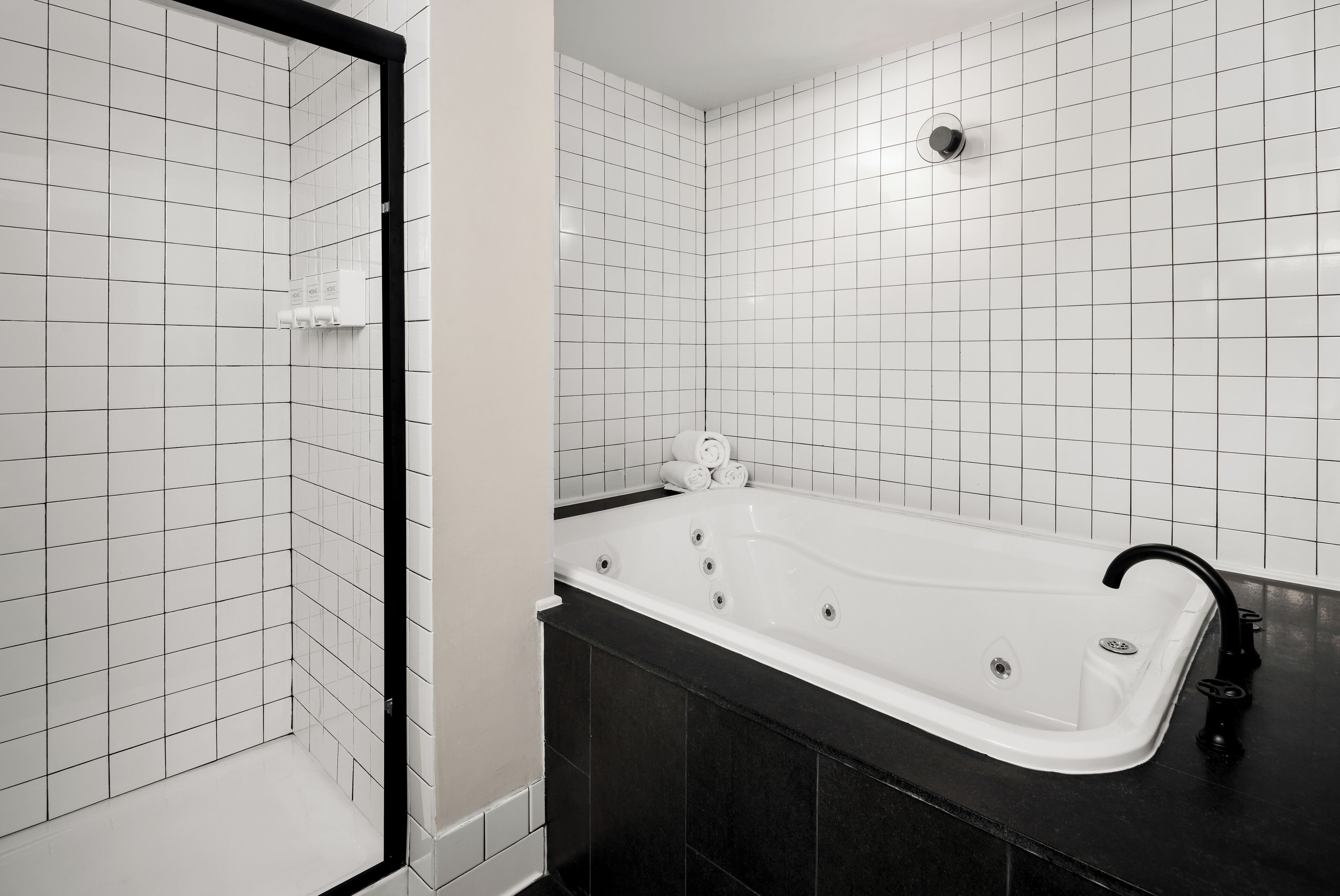 A modern bathroom with a freestanding bathtub, black countertop, and white tiled walls.