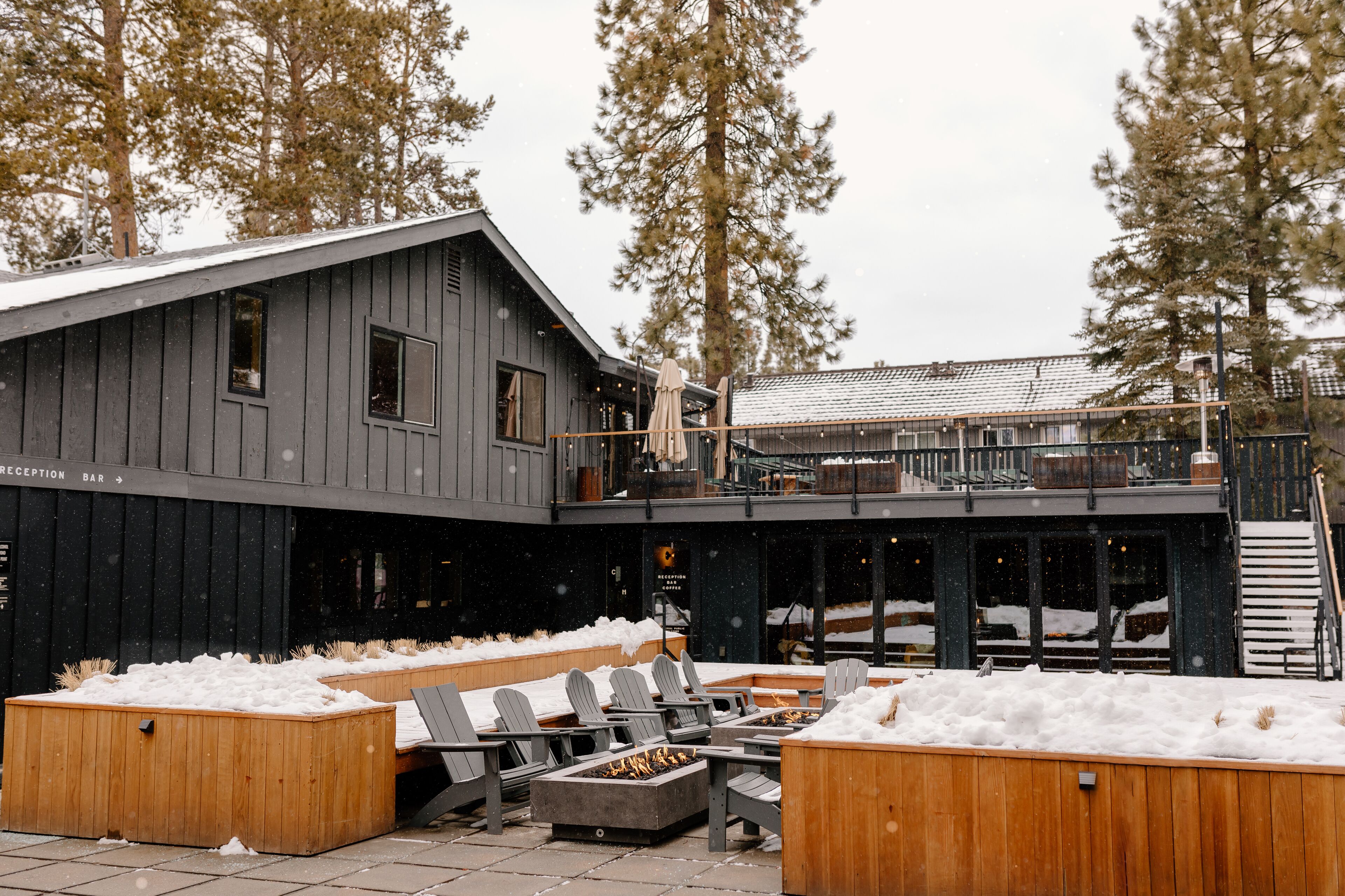 Un edificio de madera con barra de recepción, asientos exteriores con sillones Adirondack y un patio cubierto de nieve.