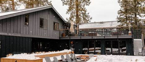 Un edificio de madera con barra de recepción, asientos exteriores con sillones Adirondack y un patio cubierto de nieve.