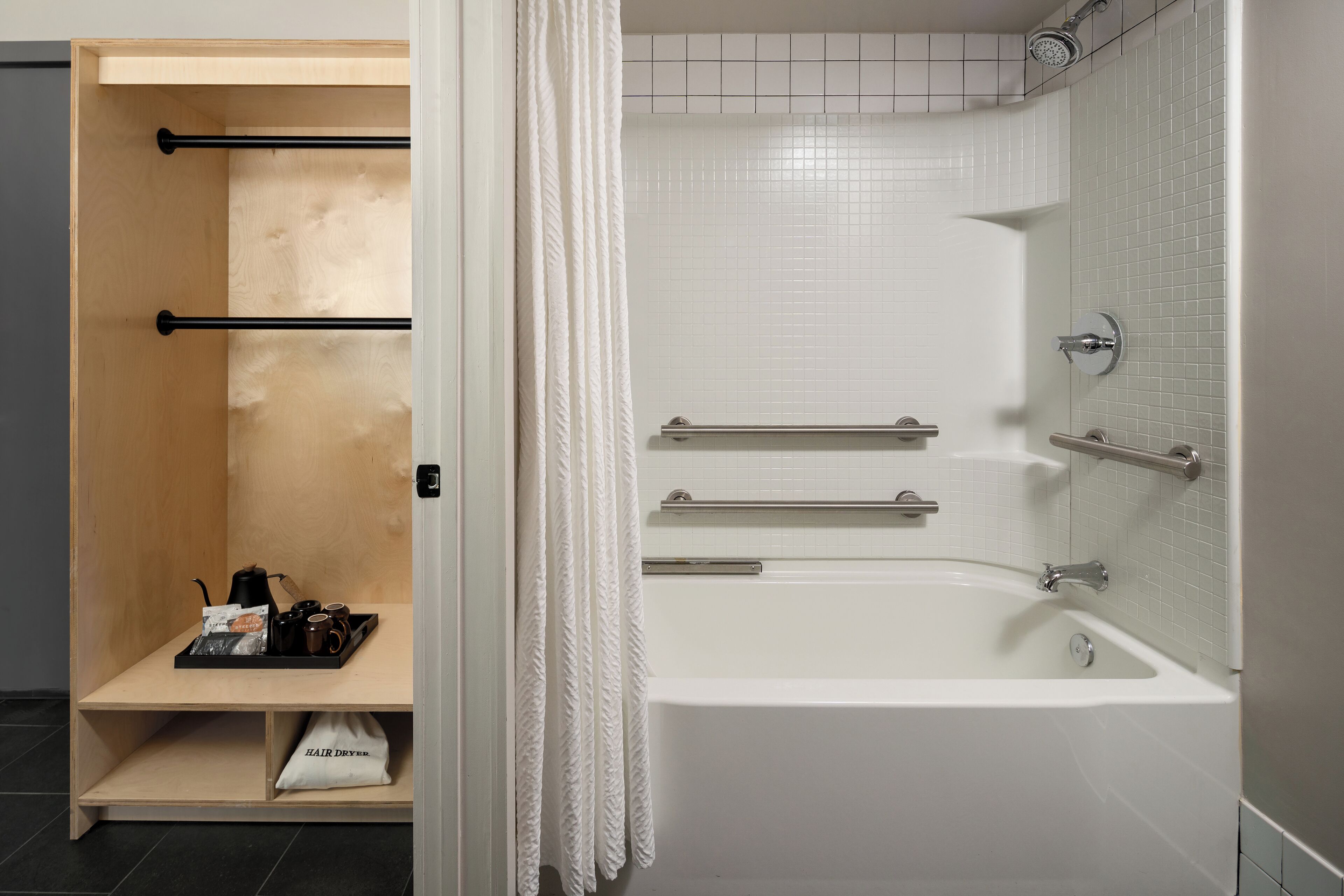 A modern bathroom with a white bathtub, a shower area, and a wooden shelf with a tea set.