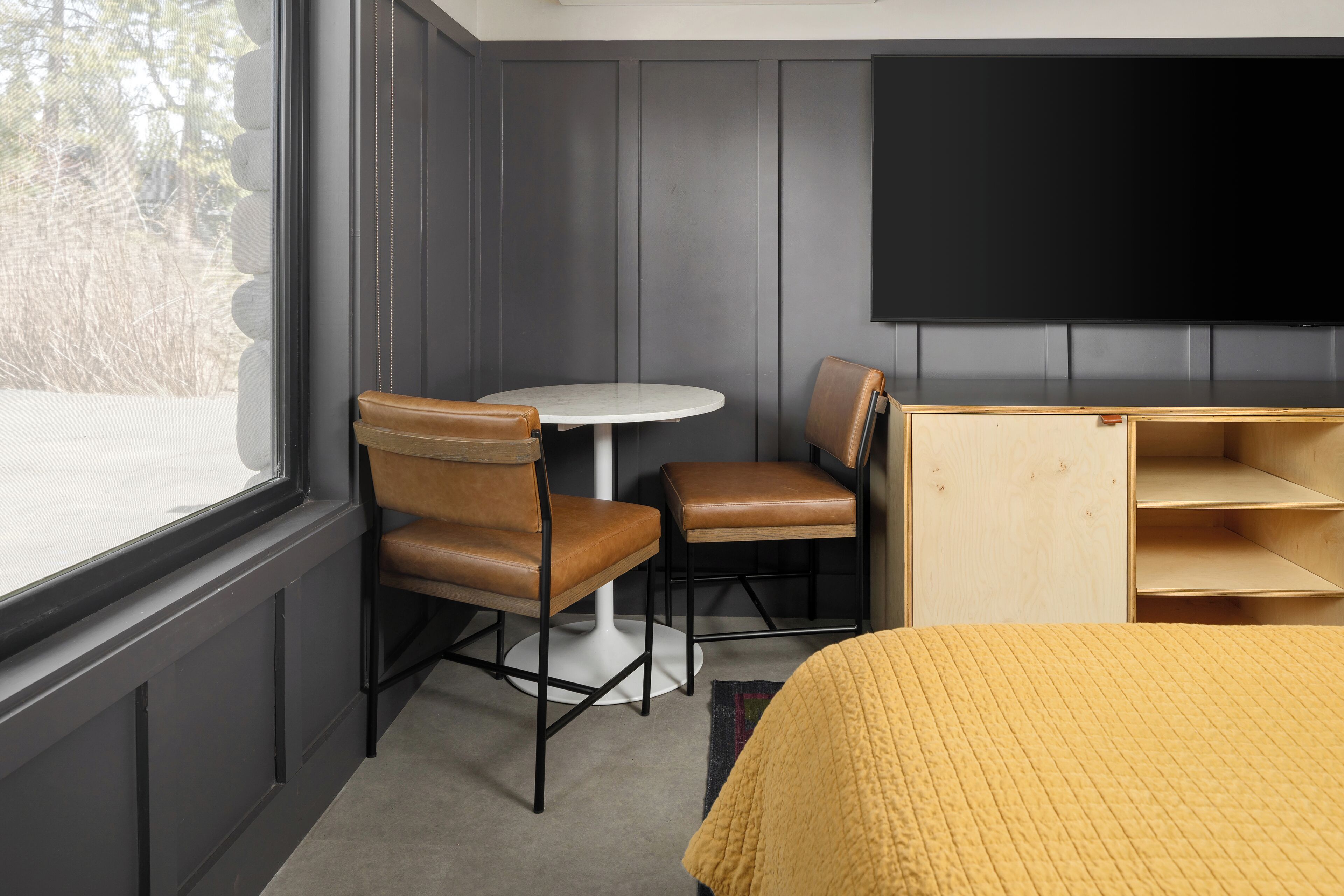 A room with a bed, a round table, two chairs, a TV, and a wooden cabinet.