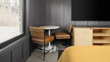 A room with a bed, a round table, two chairs, a TV, and a wooden cabinet.