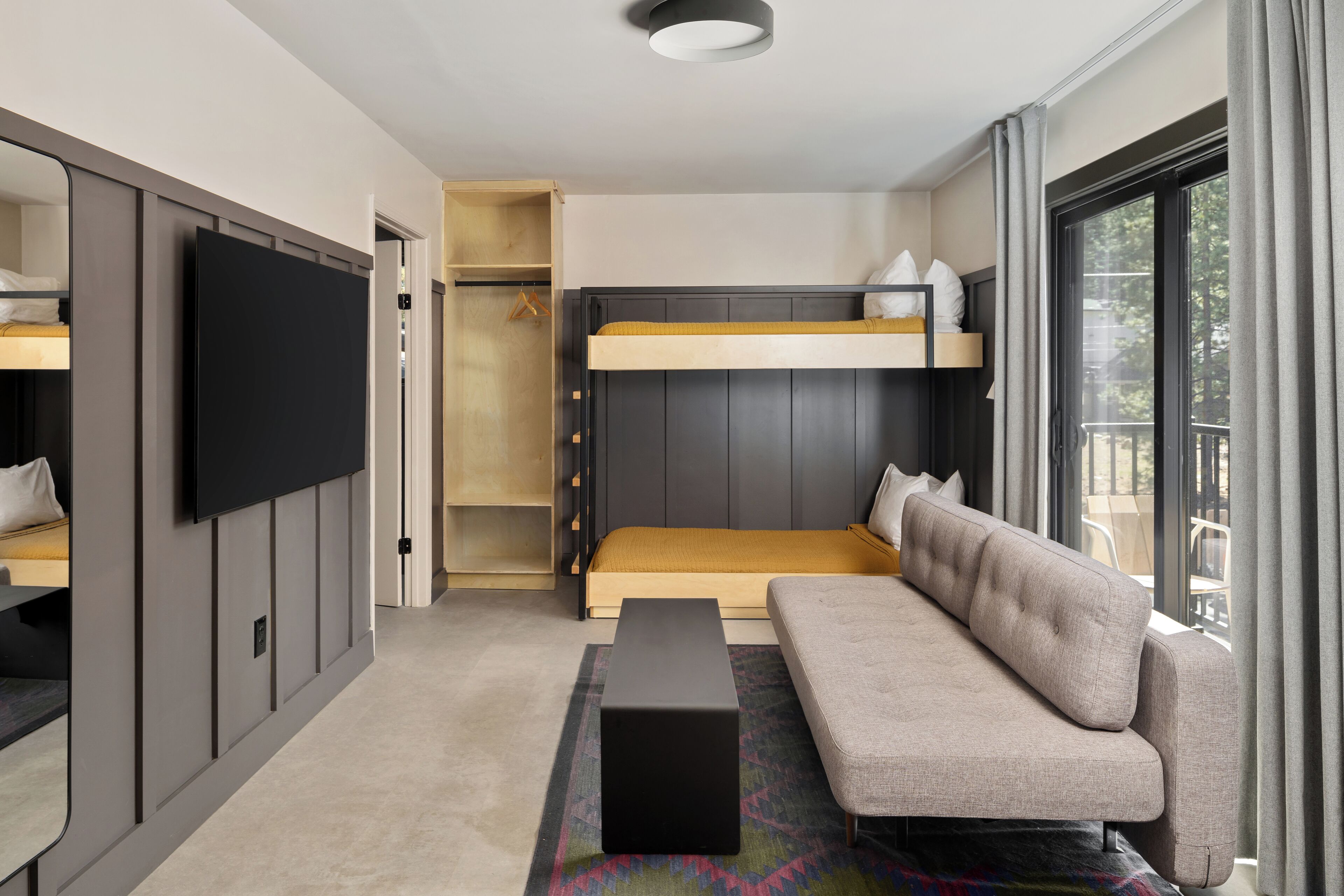 Una habitación de hotel moderna con una cama nido, un sofá, un televisor de pantalla plana y un ventanal con cortinas.