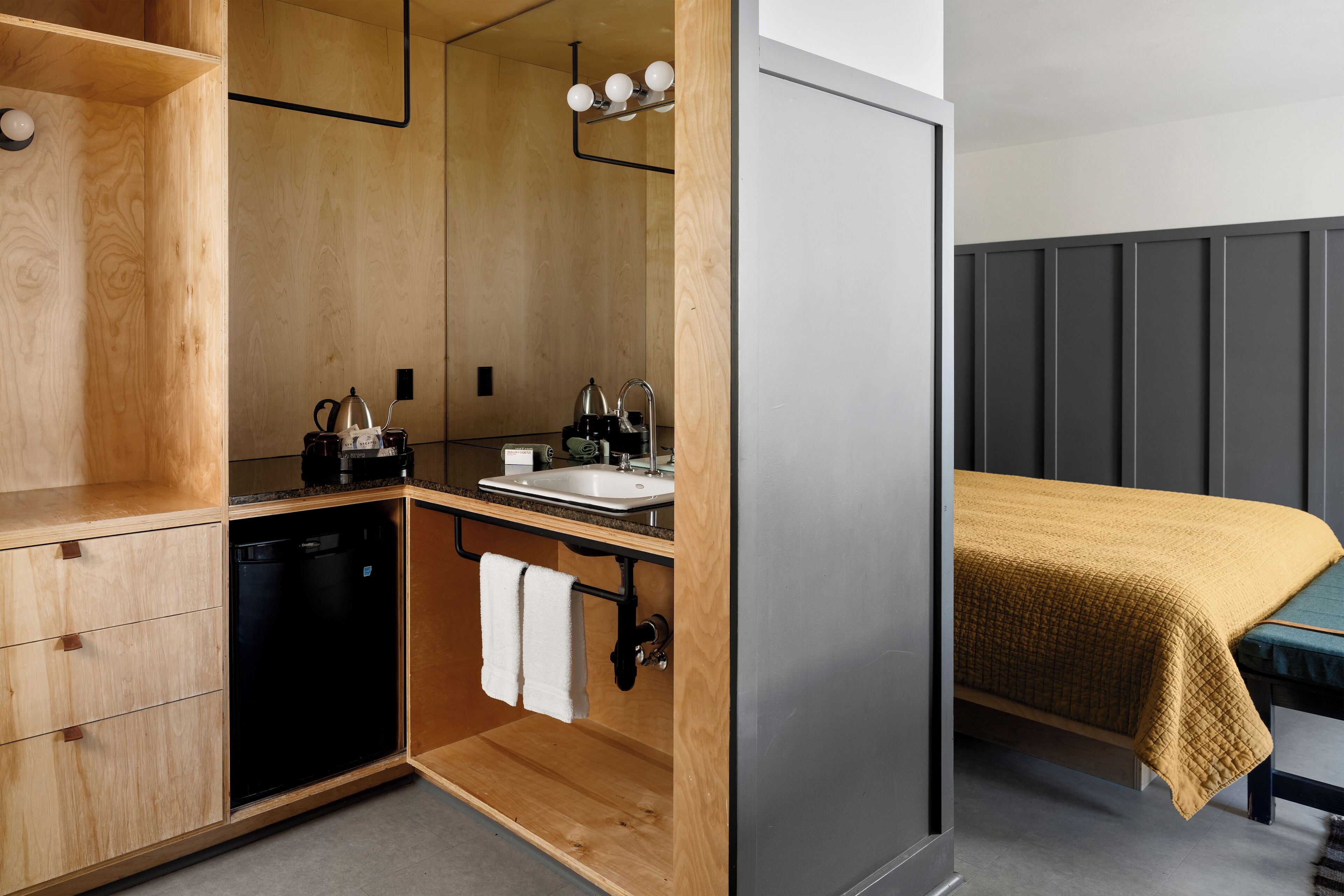 A compact room with a wooden cabinet, a sink, a small kitchen area, and a bed with a yellow blanket.