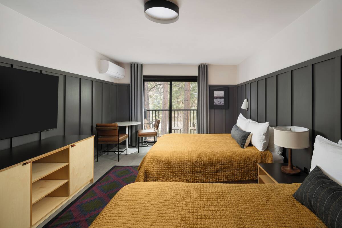 Une chambre d’hôtel avec deux lits, un bureau, une chaise, une télévision et une fenêtre donnant sur des arbres.