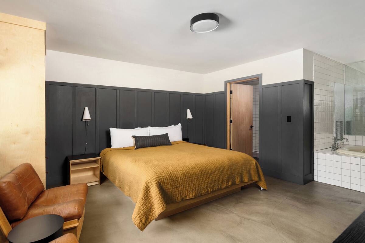 Une chambre moderne avec un grand lit, des tables de chevet, un canapé et une salle de bain dotée d’une douche en verre.