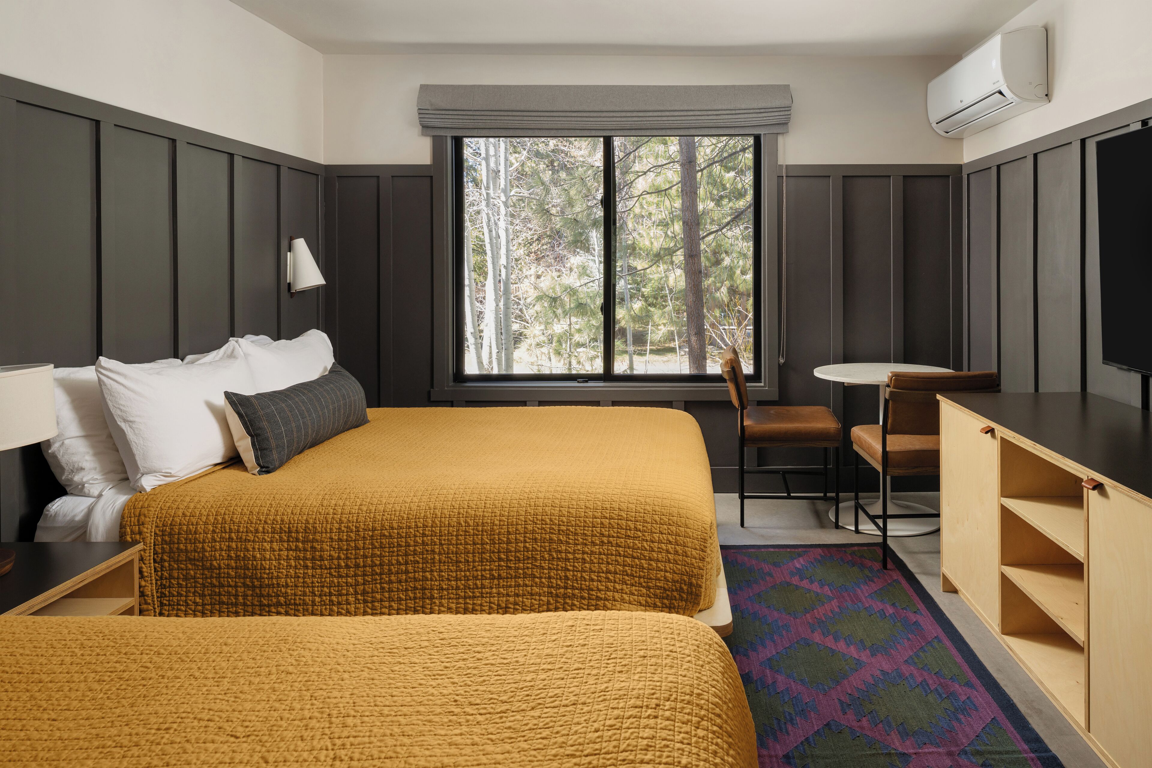 Camera d'albergo con un letto grande, una scrivania, una sedia e una finestra vista alberi.