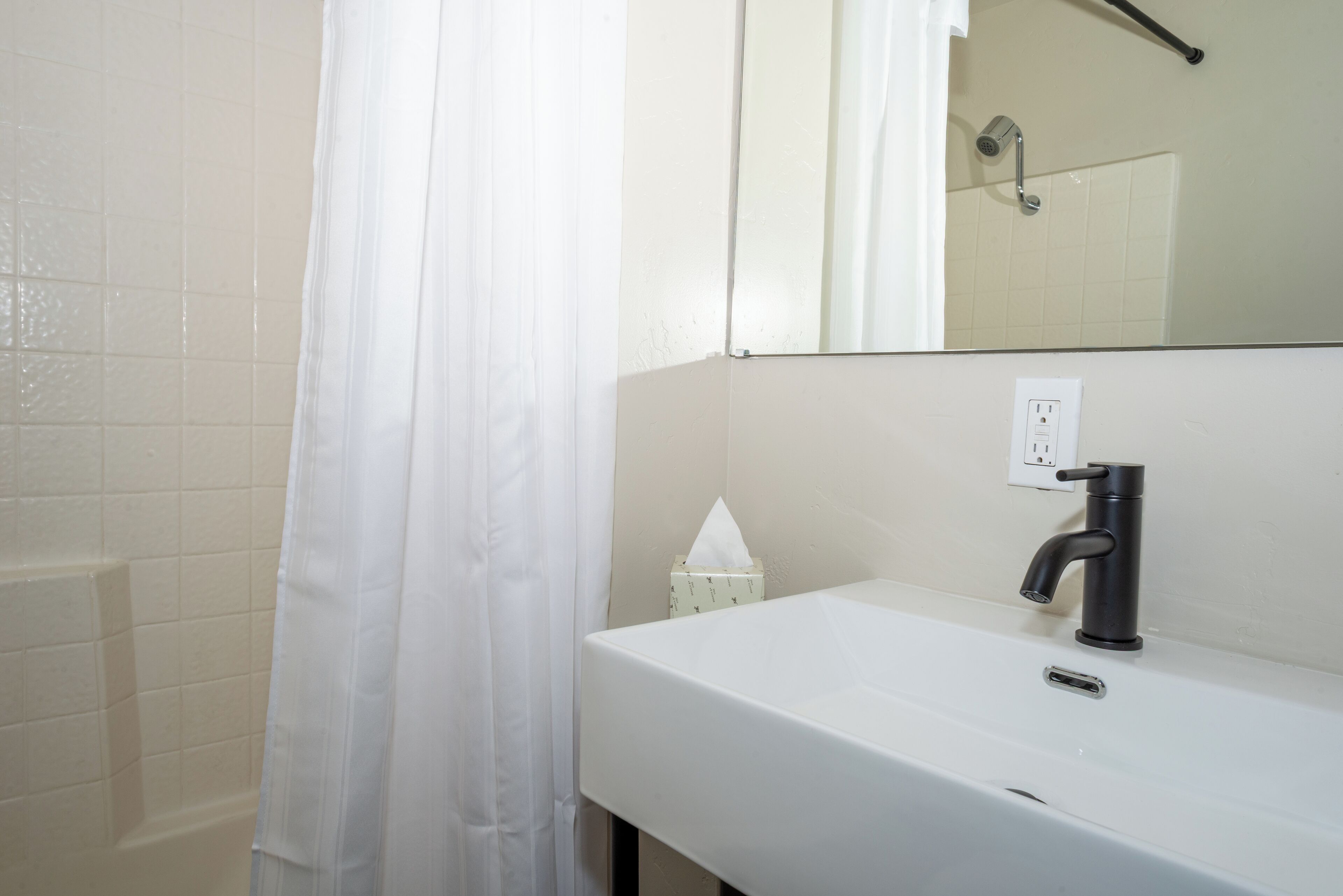 A bathroom with a white sink, a black faucet, a mirror, and a shower curtain.