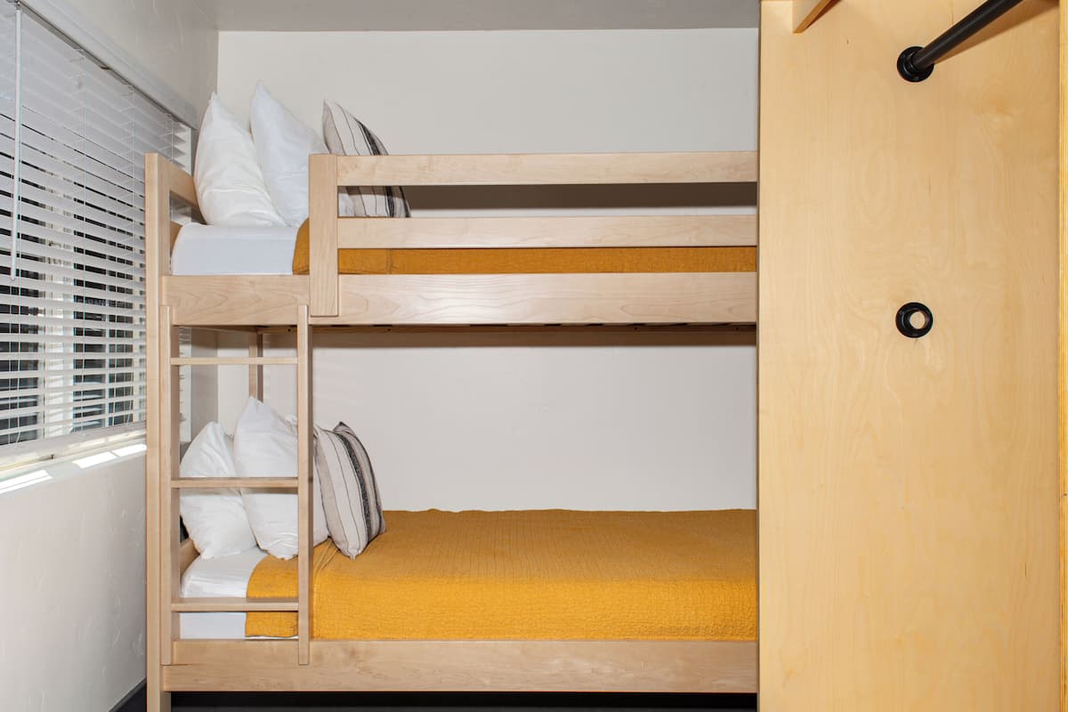 Un lit superposé avec une structure en bois, du linge de lit blanc et une couverture jaune.