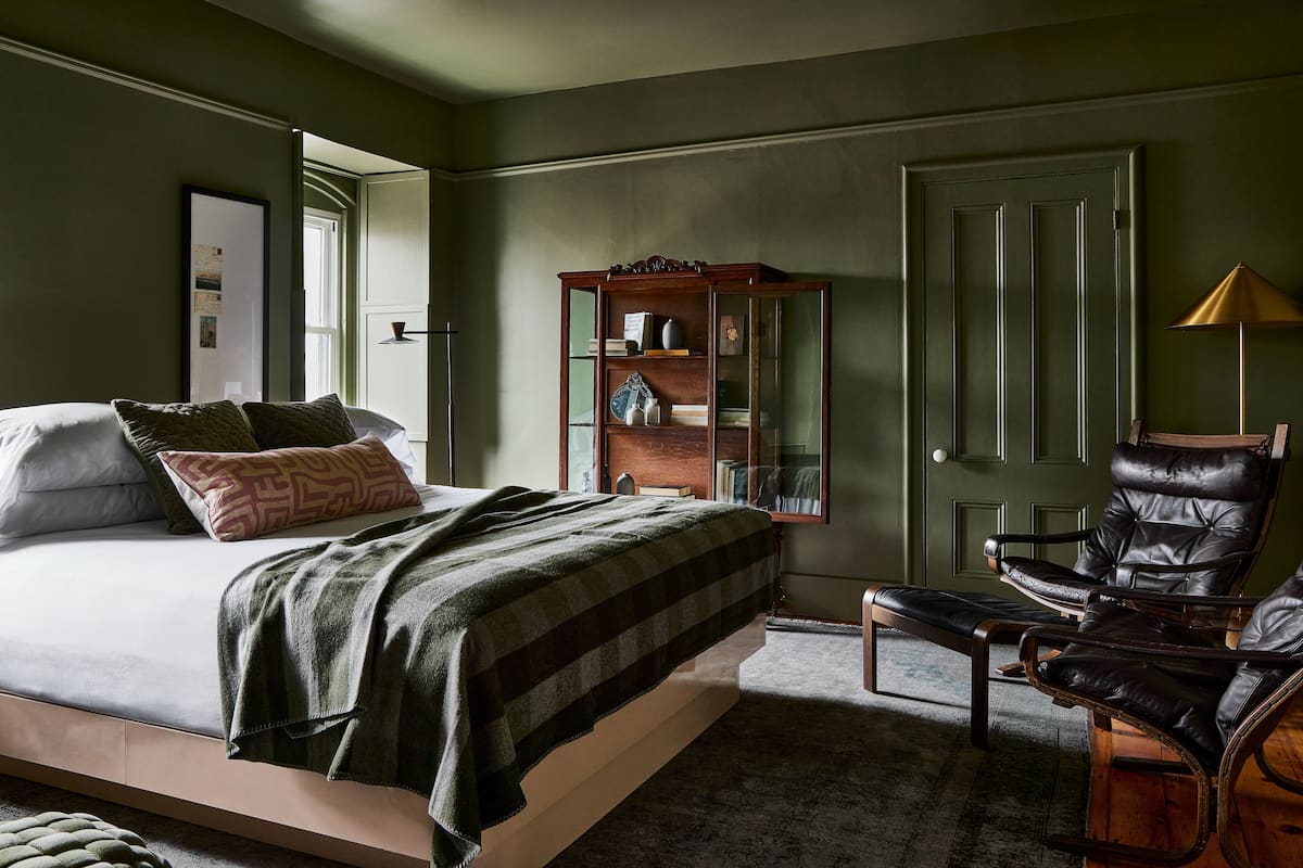 Quarto com uma cama, um armário de madeira, uma poltrona de couro e um abajur.