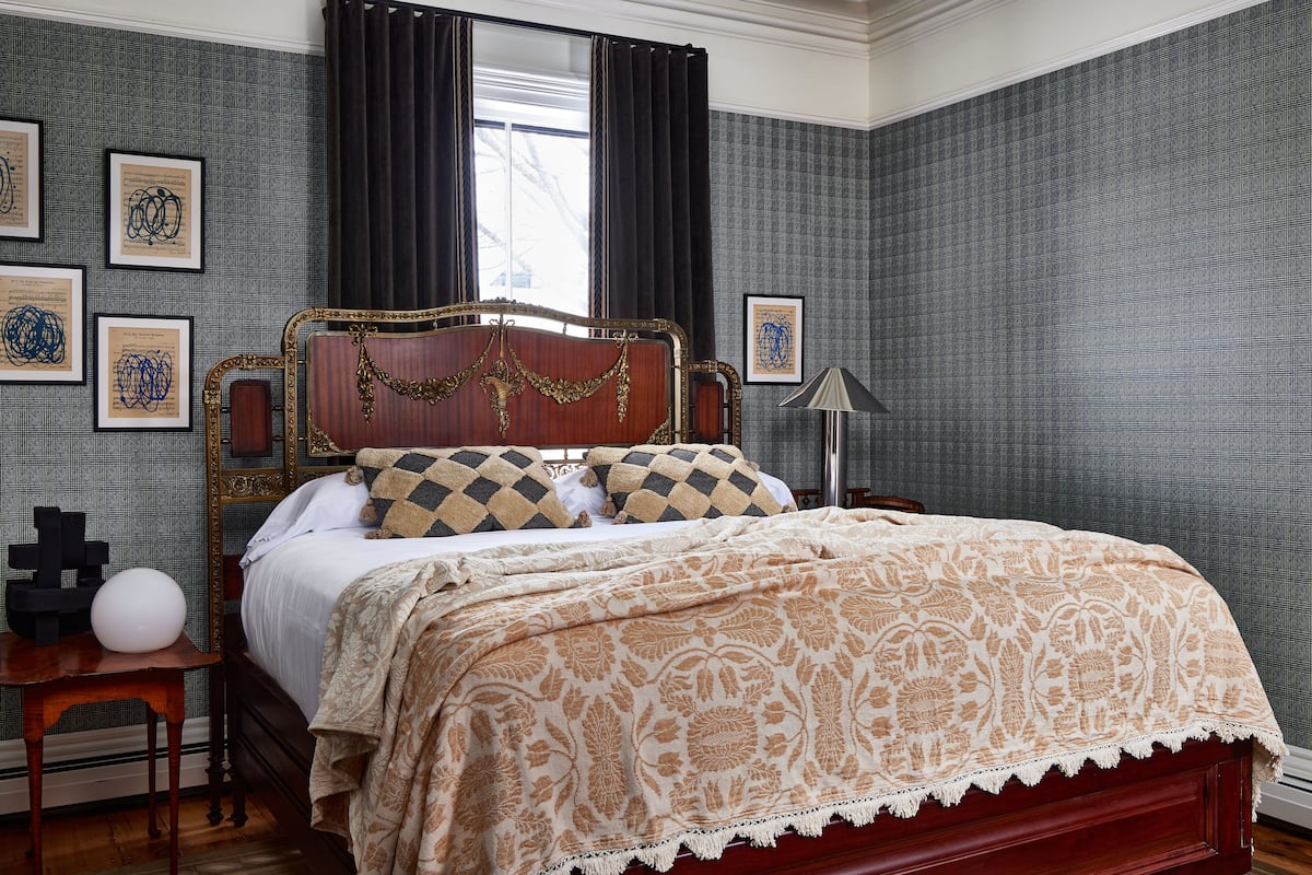 Quarto com cama de madeira, mesa de cabeceira, abajur e quadros na parede.