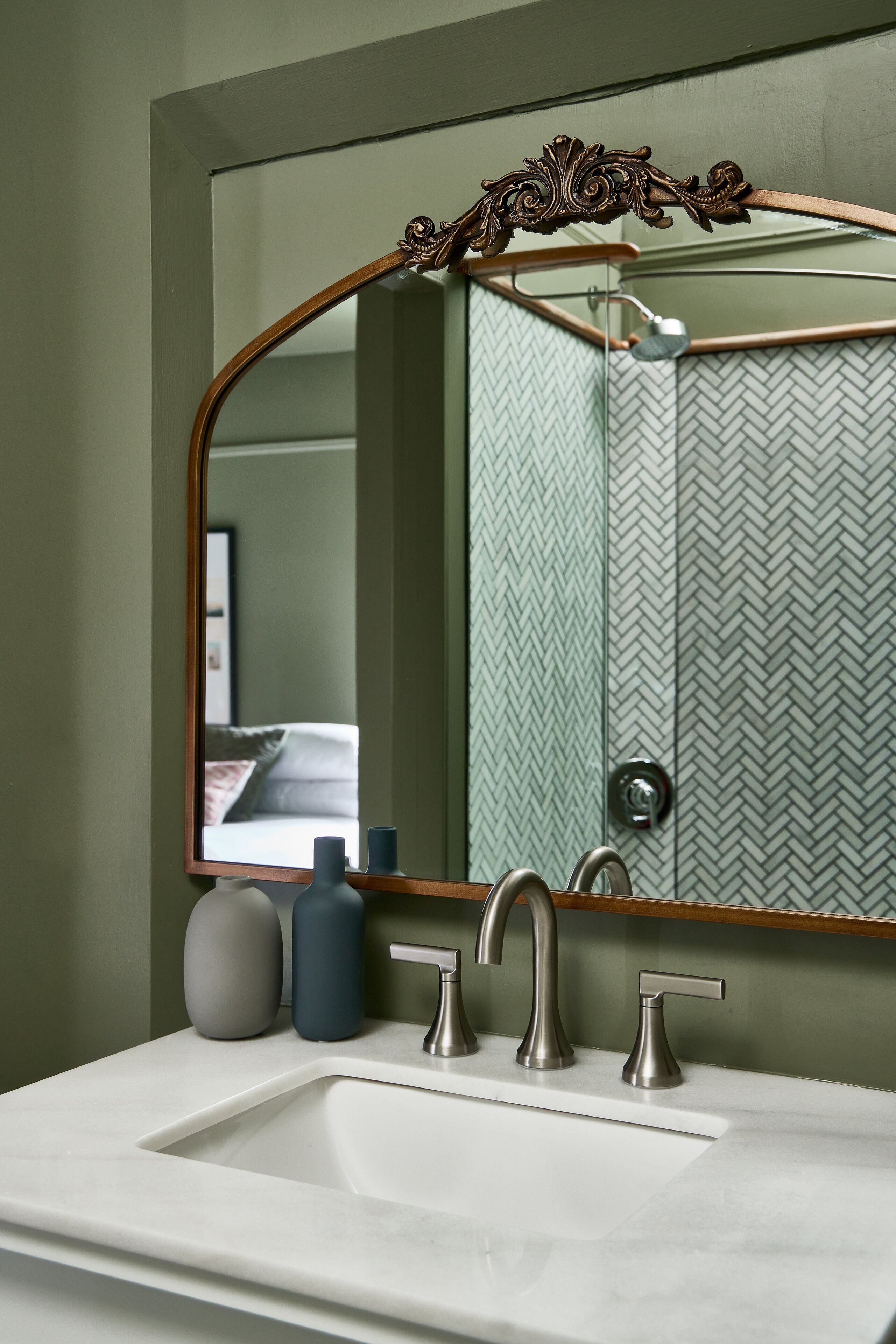 Un baño con un espejo grande, un lavamanos con dos grifos y una zona de ducha con pared de azulejos en patrón de espiga.