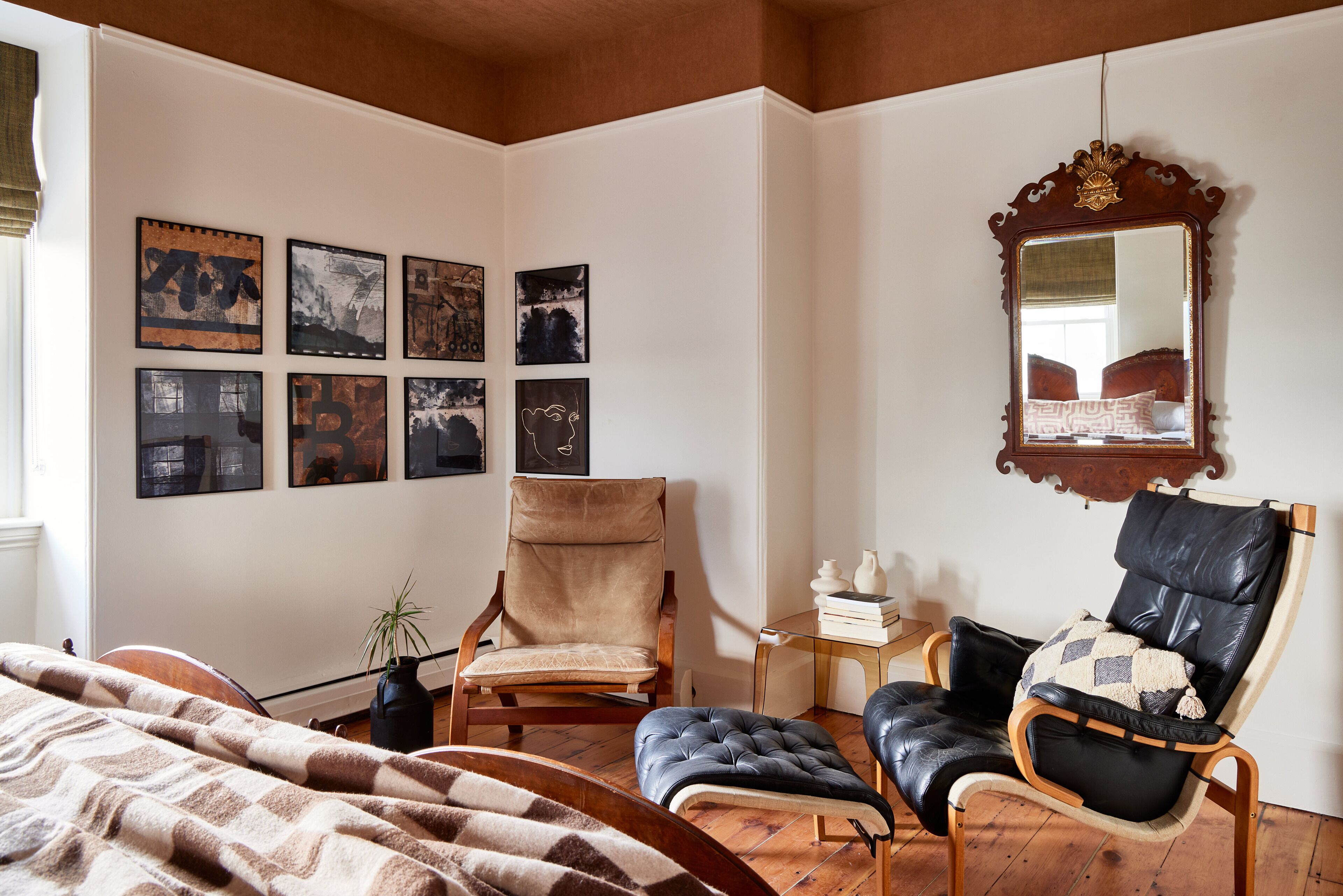 Quarto com cama, duas cadeiras, espelho e decoração nas paredes.