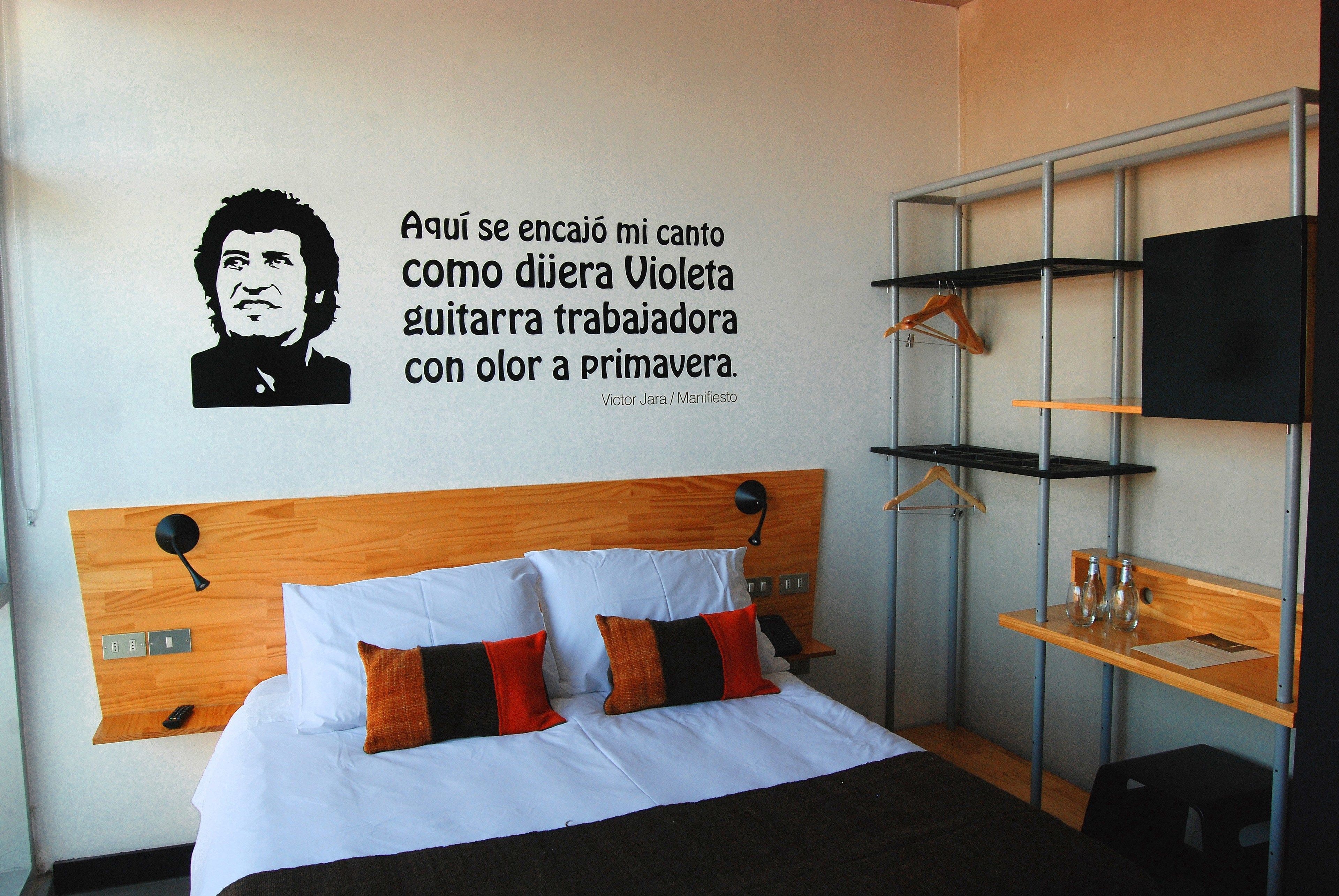 Une chambre d’hôtel avec un lit, une citation accrochée au mur et un téléviseur posé sur une étagère.
