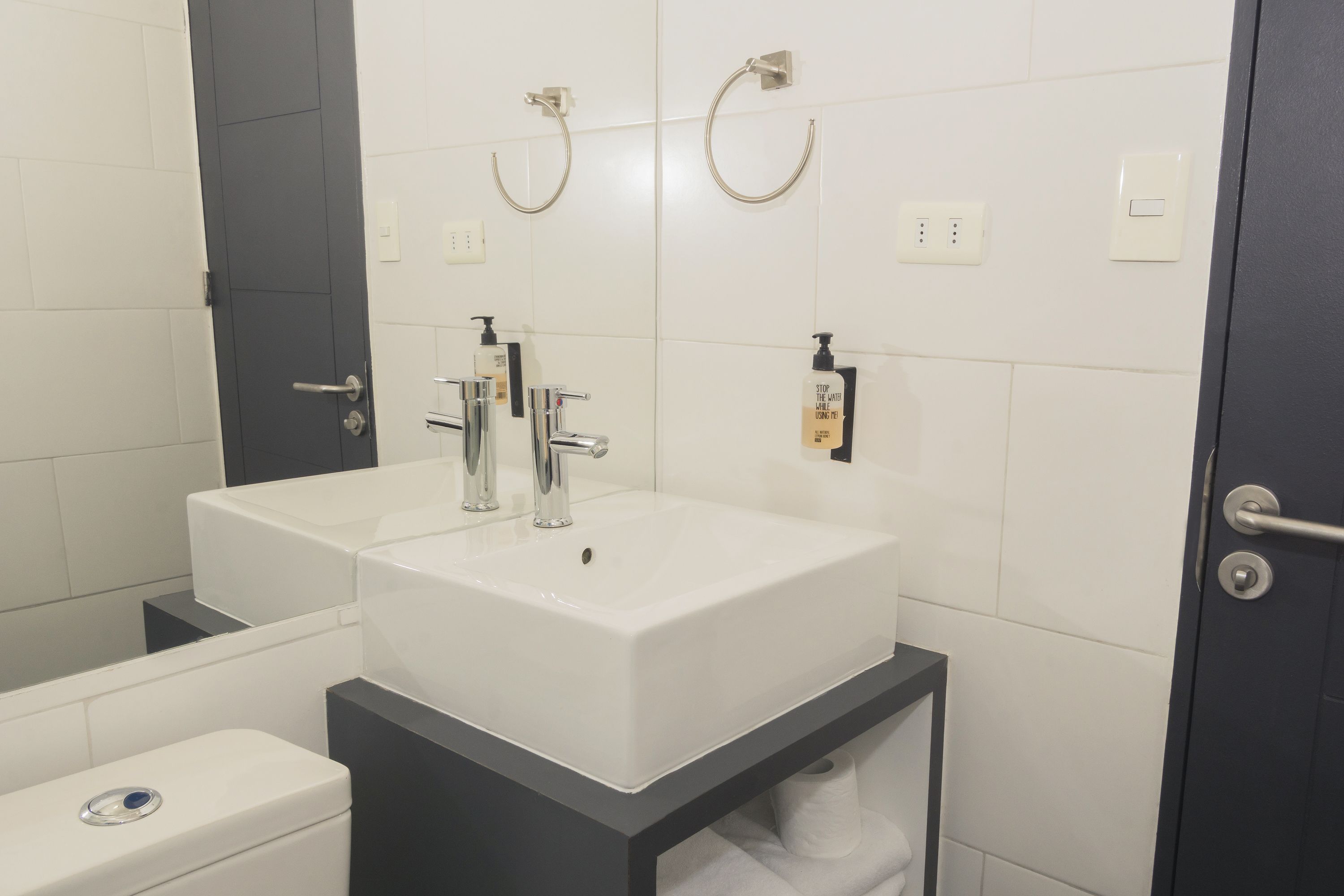 Un baño moderno con un lavamanos blanco, un inodoro y un mueble de baño oscuro.