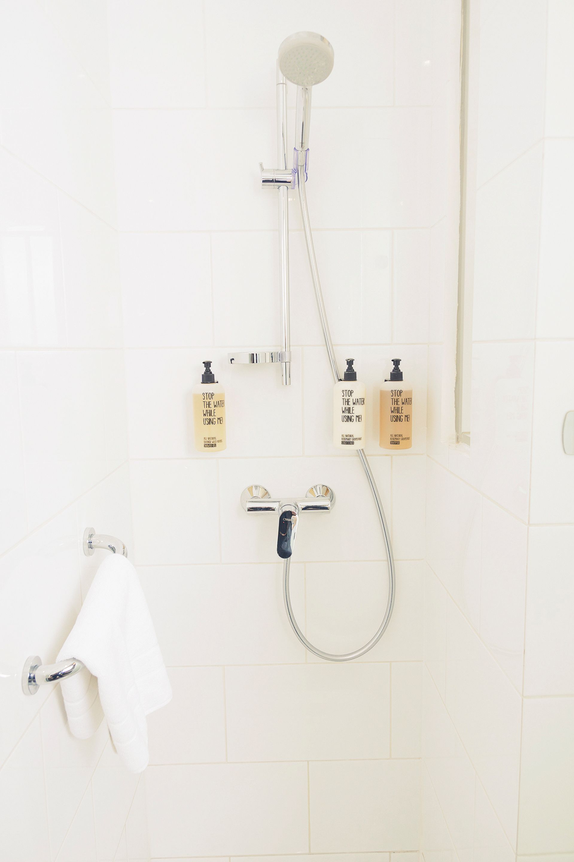Une salle de bain avec une douche, deux distributeurs de savon et un porte-serviettes.