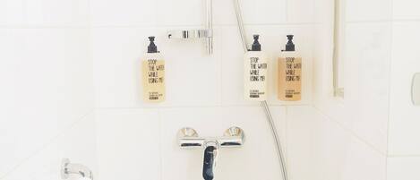 Une salle de bain avec une douche, deux distributeurs de savon et un porte-serviettes.