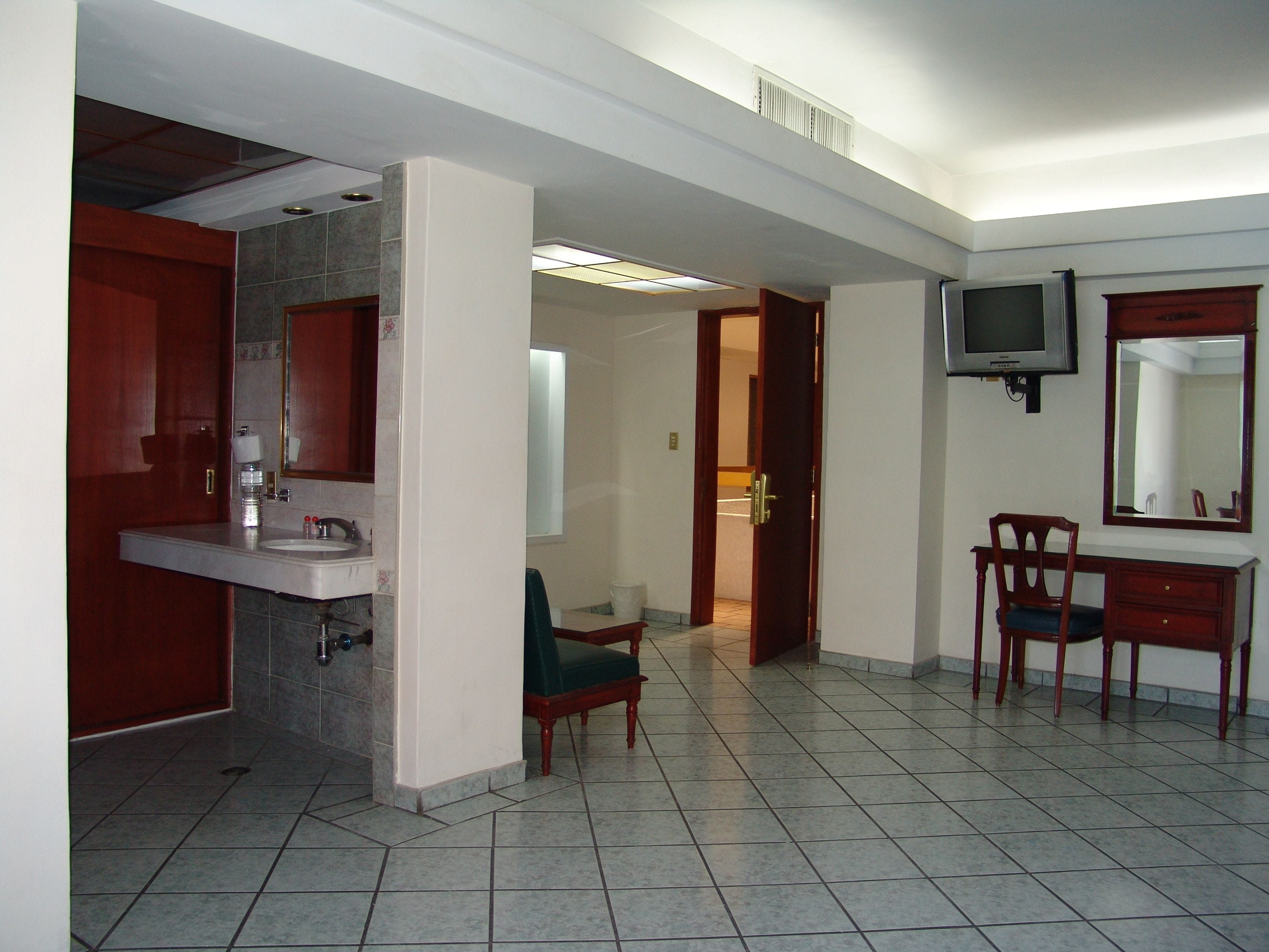 A hotel room with a bathroom, a television, and a desk with a chair.