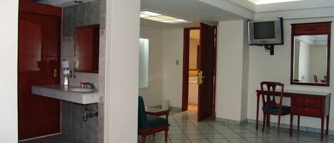 A hotel room with a bathroom, a television, and a desk with a chair.
