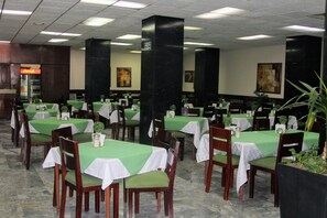 A restaurant with multiple tables covered in green tablecloths and wooden chairs.