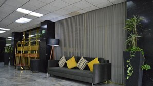 Un vestíbulo con un sofá gris, cojines negros y amarillos, una lámpara de pie alta y una planta en maceta.