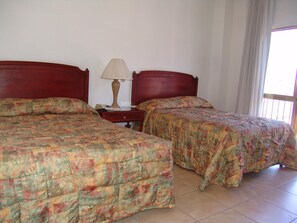 A hotel room with two beds, a nightstand, a lamp, and a window with curtains.