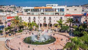 Un hotel con una fuente central, rodeado de palmeras y una plaza adoquinada.