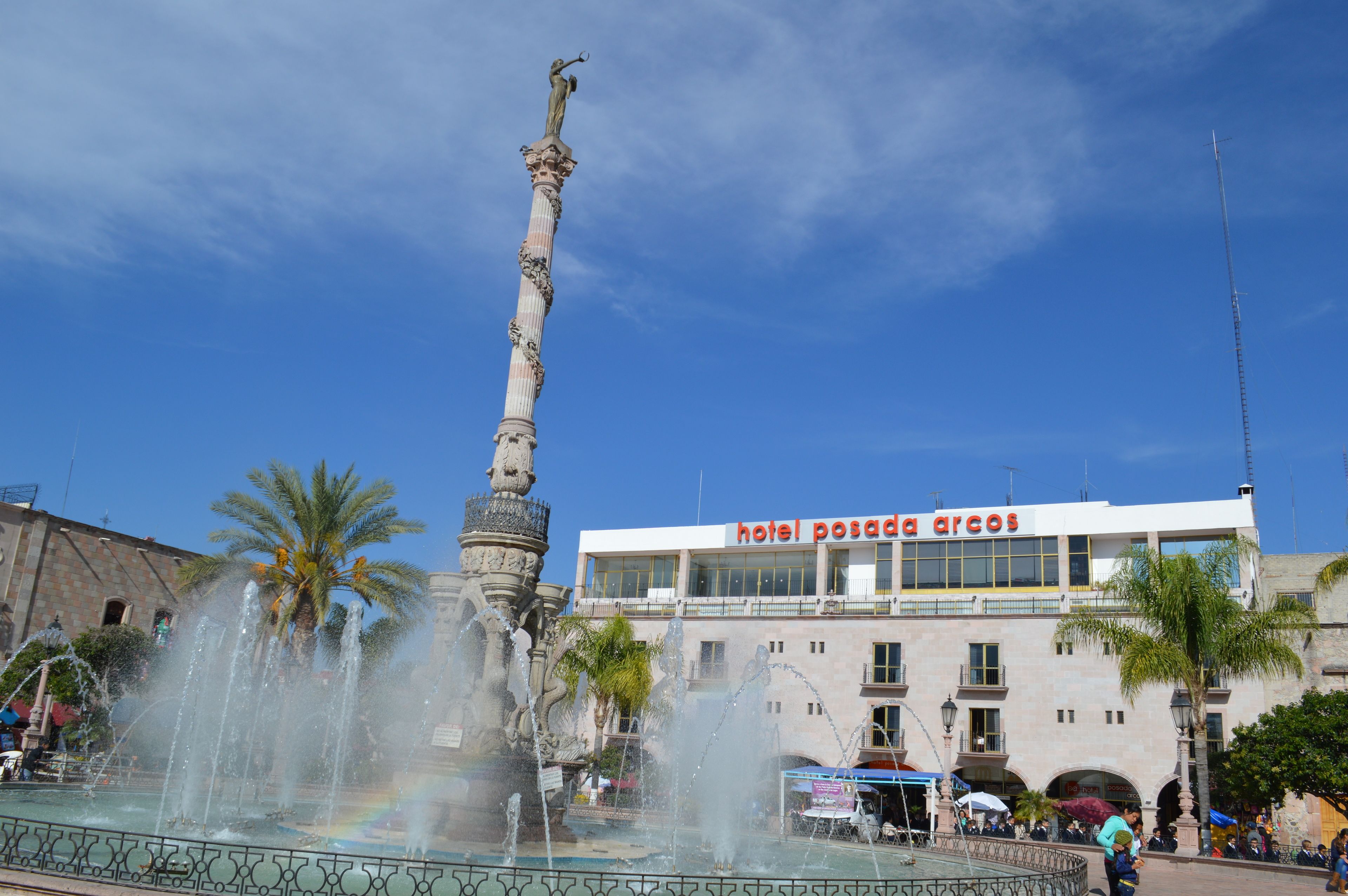 A hotel with a fountain and palm trees in front.