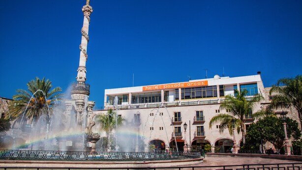 Una fuente con una estatua, un edificio con el letrero "hotel posada arcus" y palmeras.