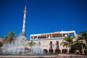 Una fuente con una estatua, un edificio con el letrero "hotel posada arcus" y palmeras.