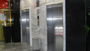 Un hall con piso de mármol, dos ascensores, un cesto de basura y un letrero que indica un área de plantas.