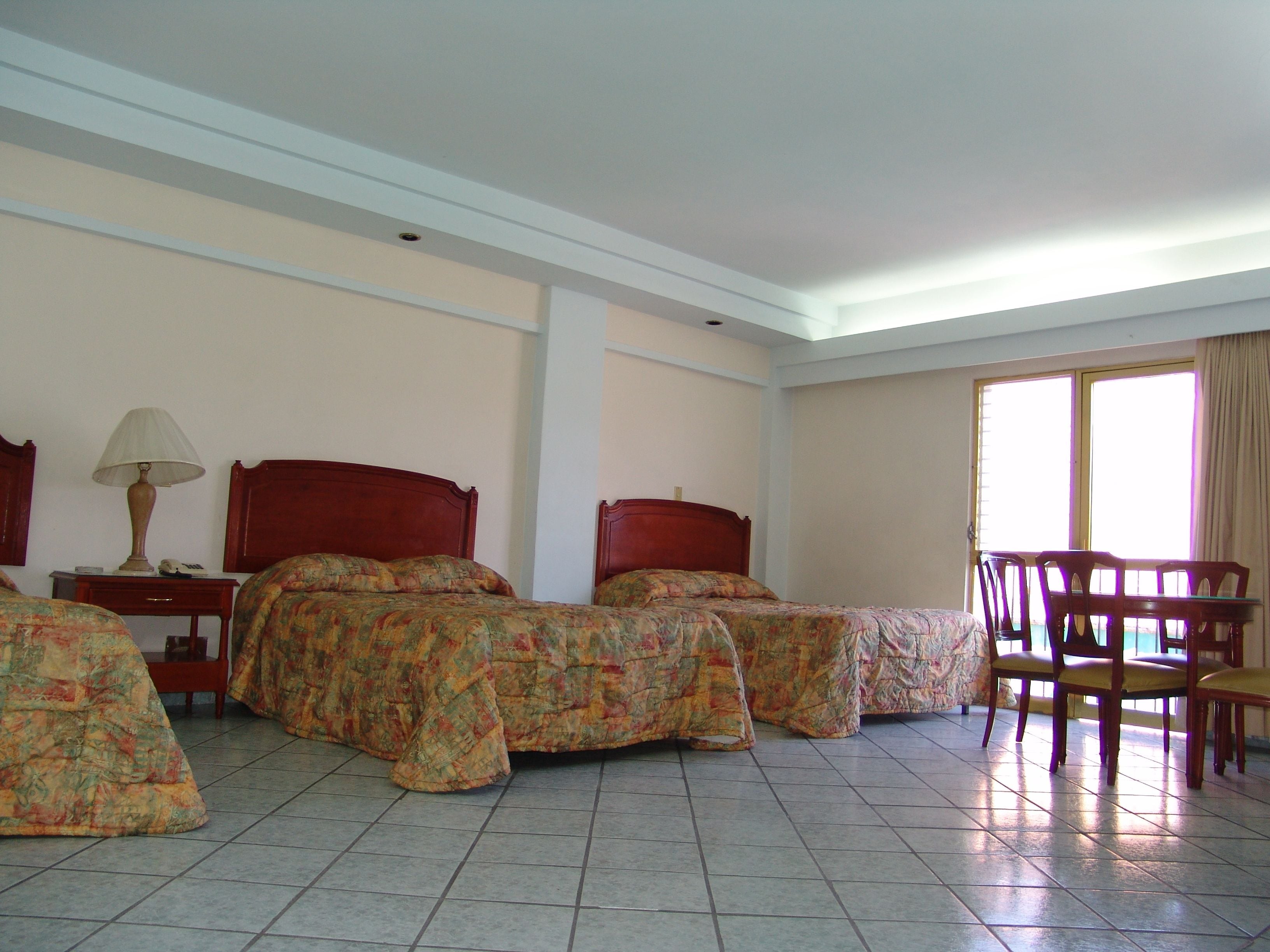A hotel room with two beds, a table, chairs, and a window.