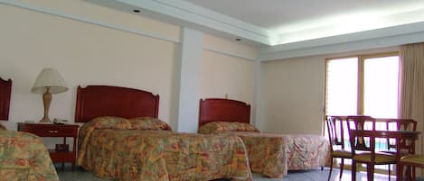 A hotel room with two beds, a table, chairs, and a window.