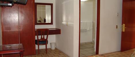 A hotel room with a bed, a desk with a chair, a television, and a bathroom visible through an open door.