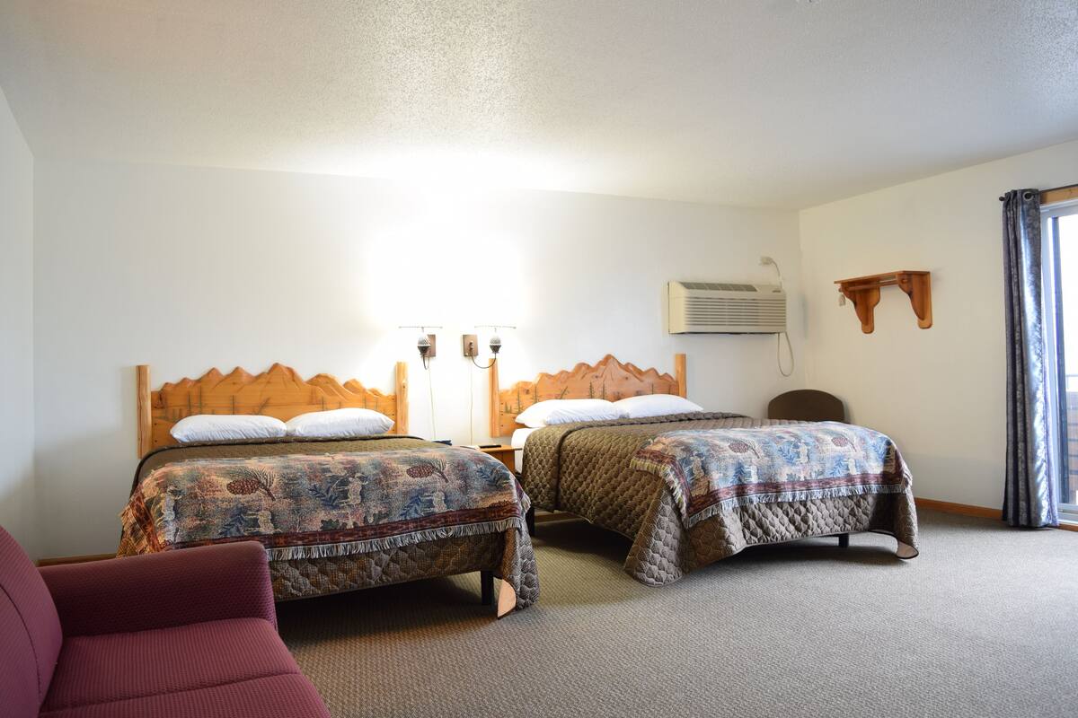 A hotel room with two beds, a wooden headboard, a red chair, and a window with curtains.