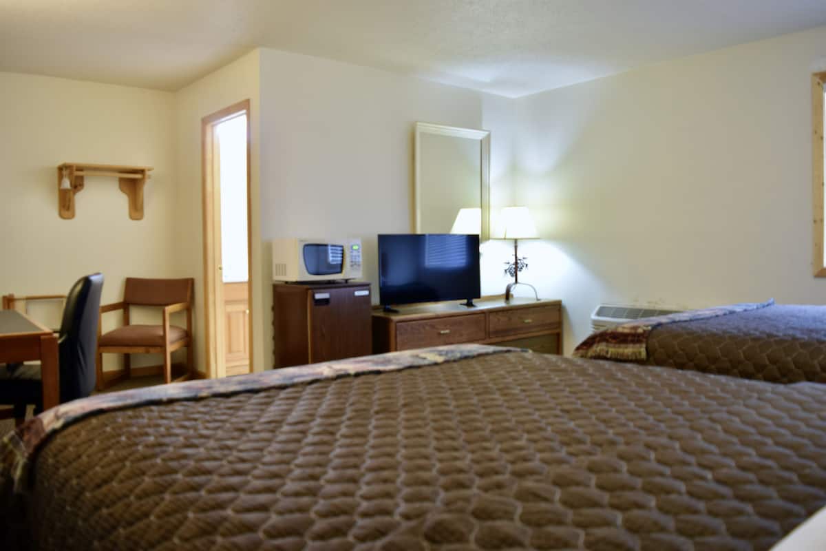 A hotel room with two beds, a desk with a chair, a television, a lamp, and a mirror.