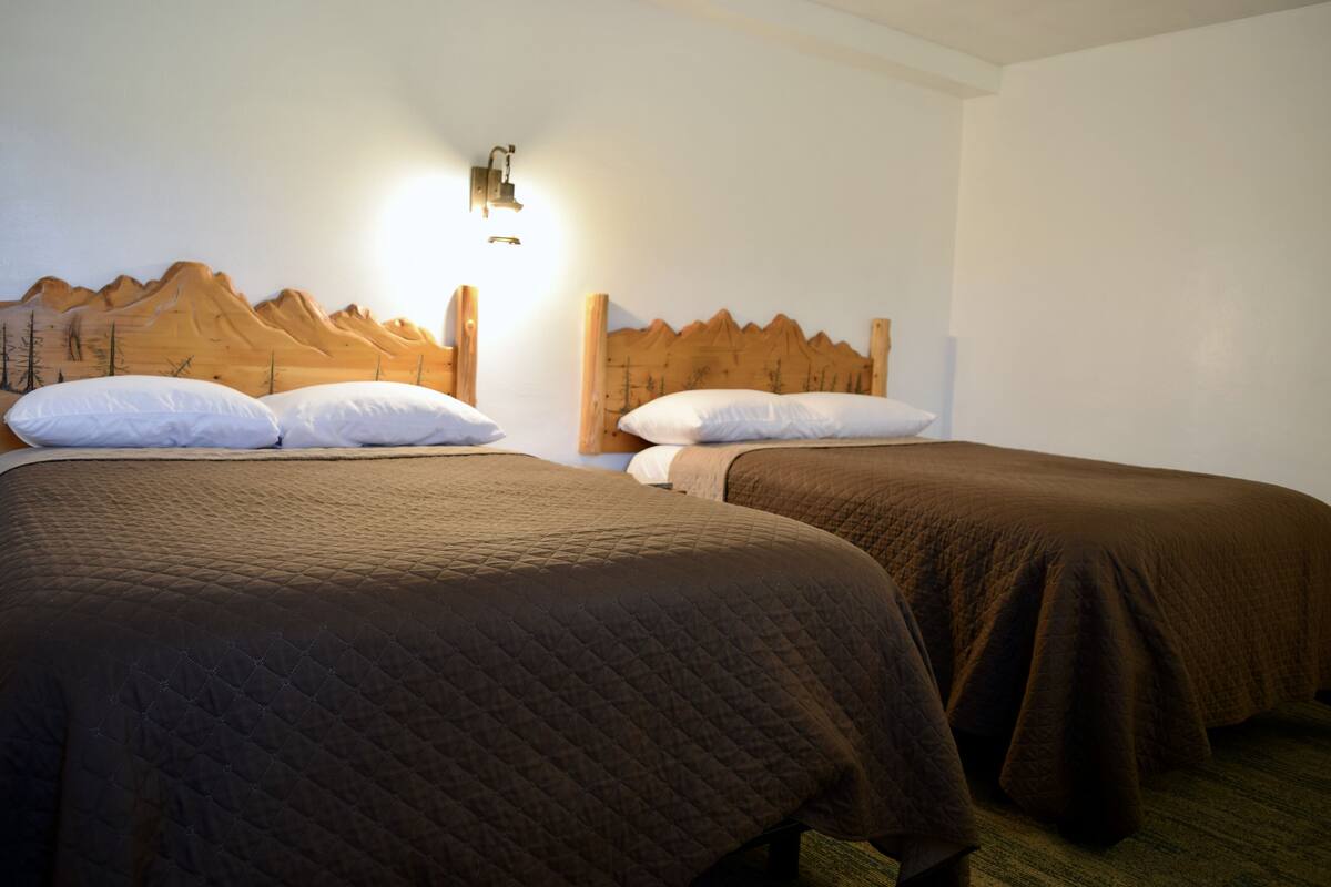 Two beds with wooden headboards, a wall-mounted light, and a mountain mural.