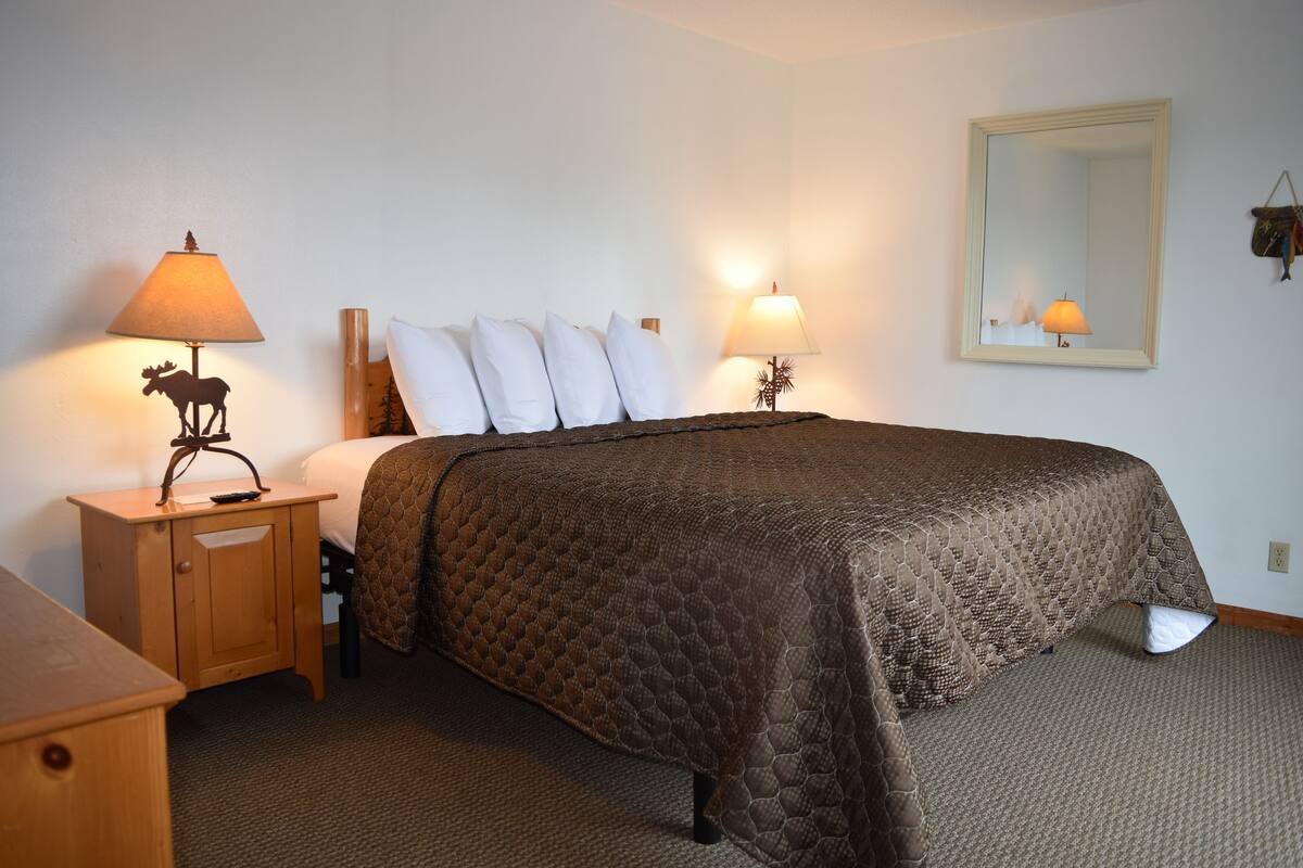 A neatly made bed with a brown quilt, two bedside lamps, a wooden nightstand, and a mirror on the wall.