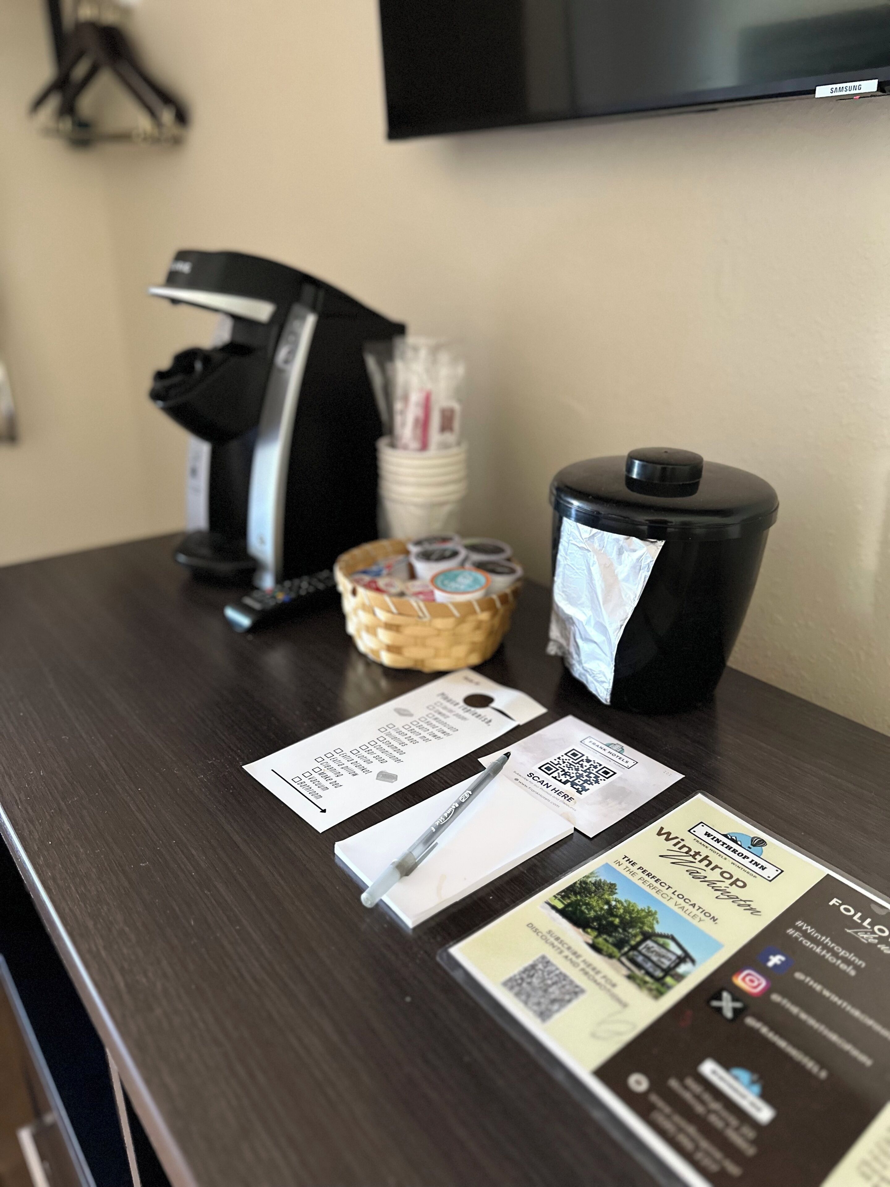 Un comptoir d’accueil d’hôtel équipé d’une machine à café, d’un panier contenant des articles de toilette et de brochures d’information.