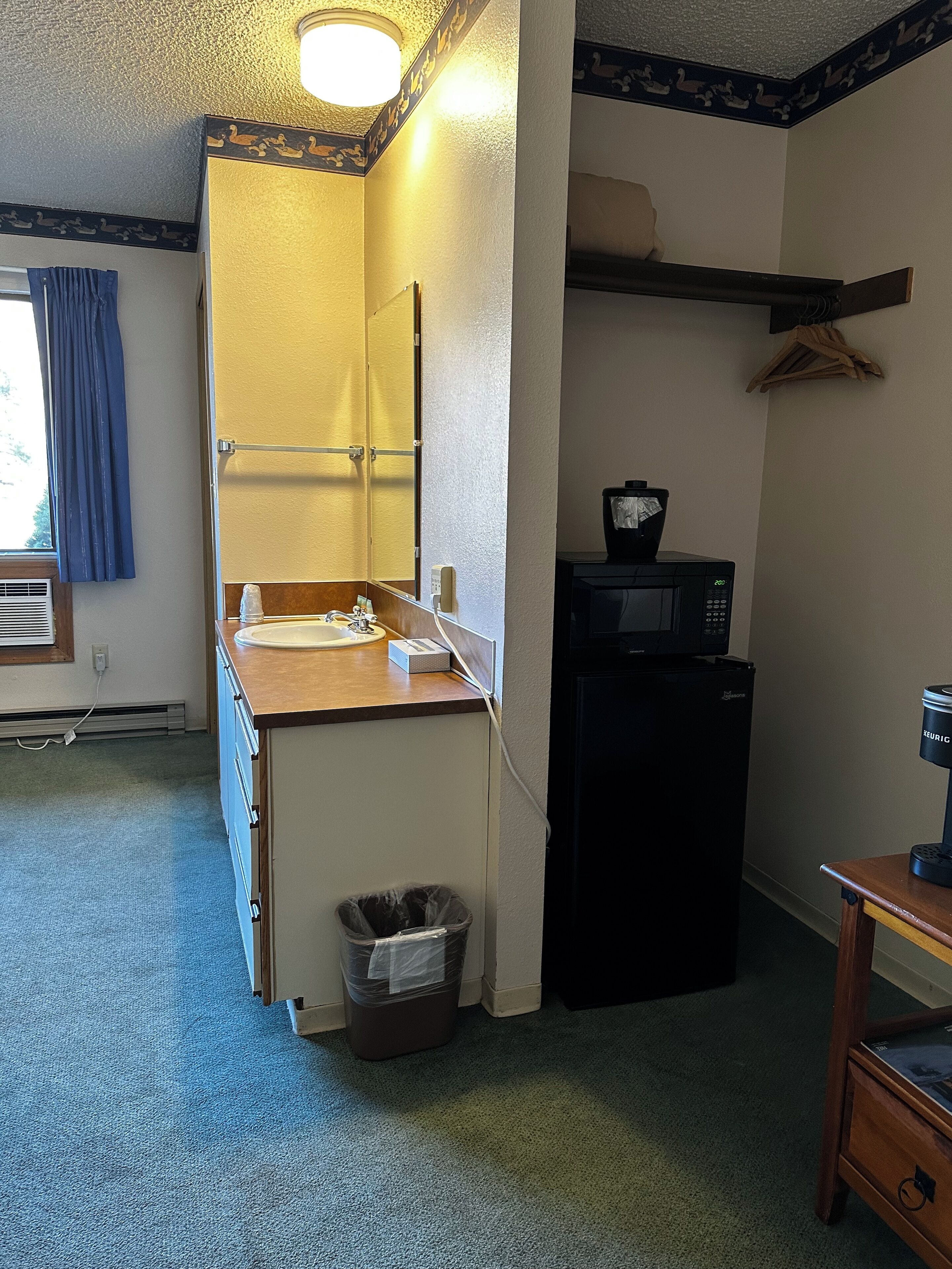 A compact kitchenette with a sink, mirror, and a microwave.
