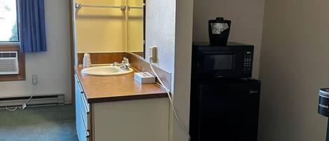 Una kitchenette compacta con un lavamanos, espejo y microondas.