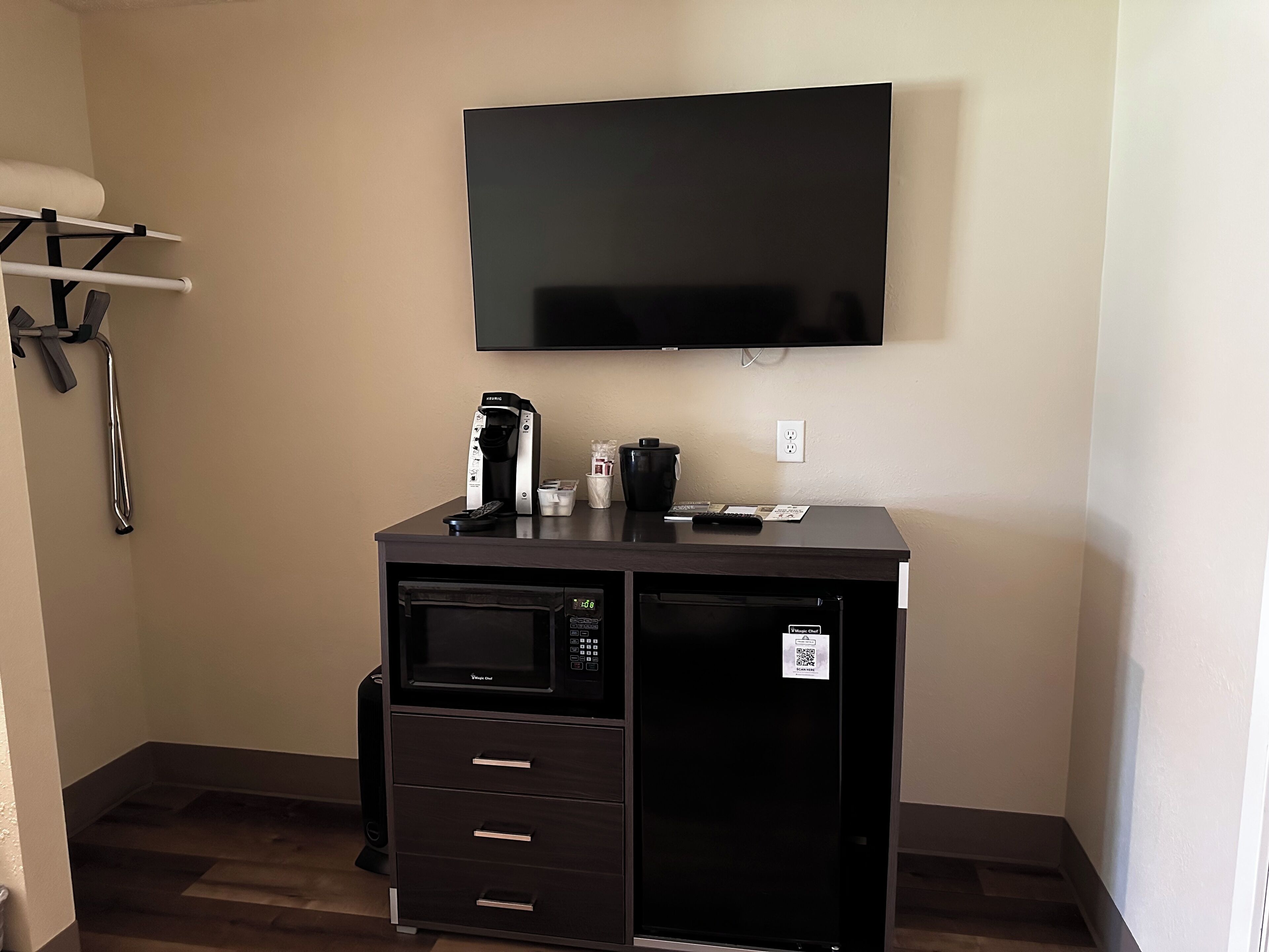 A compact kitchenette with a microwave, coffee maker, and a small refrigerator. A flat-screen TV is mounted on the wall above the counter.