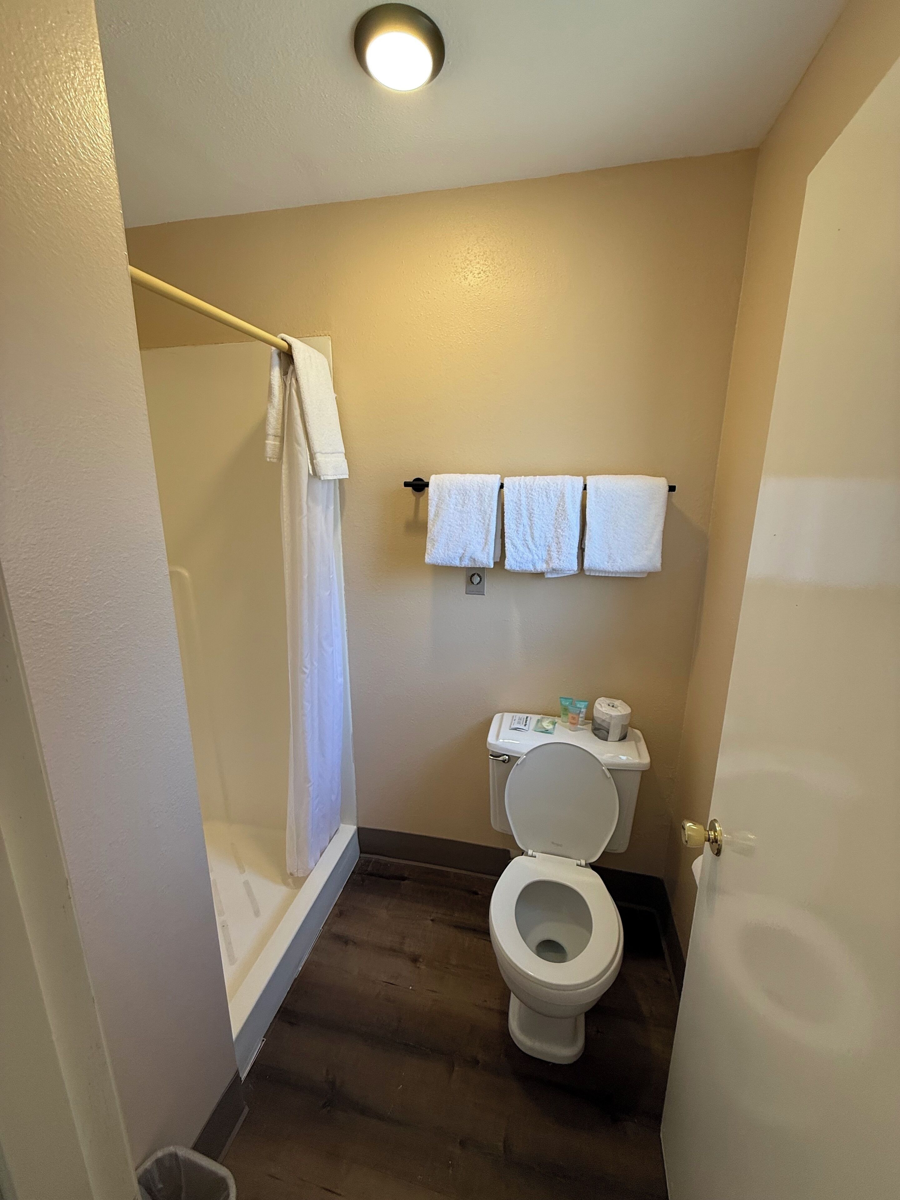 A bathroom with a toilet, a shower with a curtain, and a towel rack with three towels.