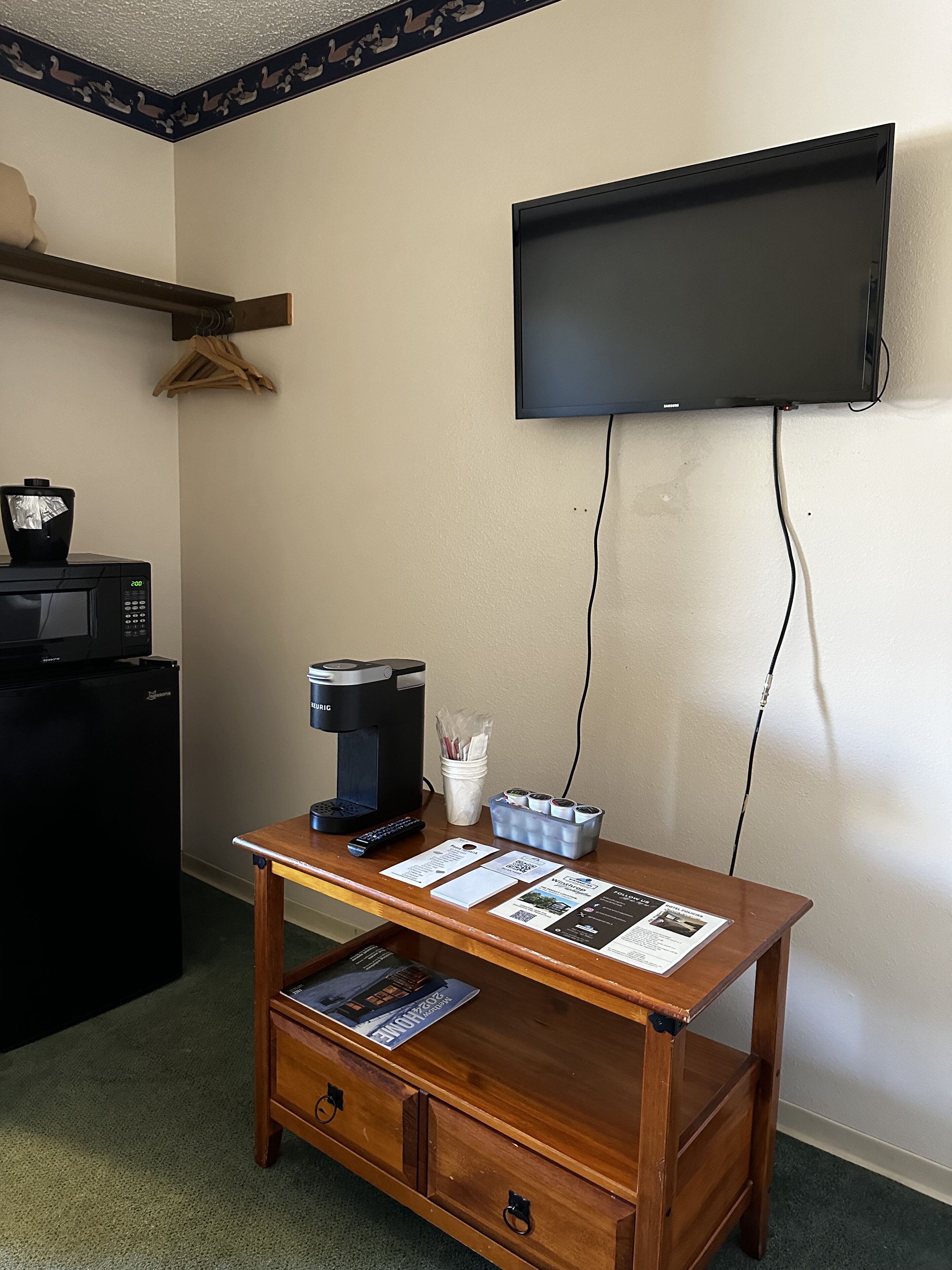 A small kitchenette with a microwave, coffee maker, and a wooden table with brochures.