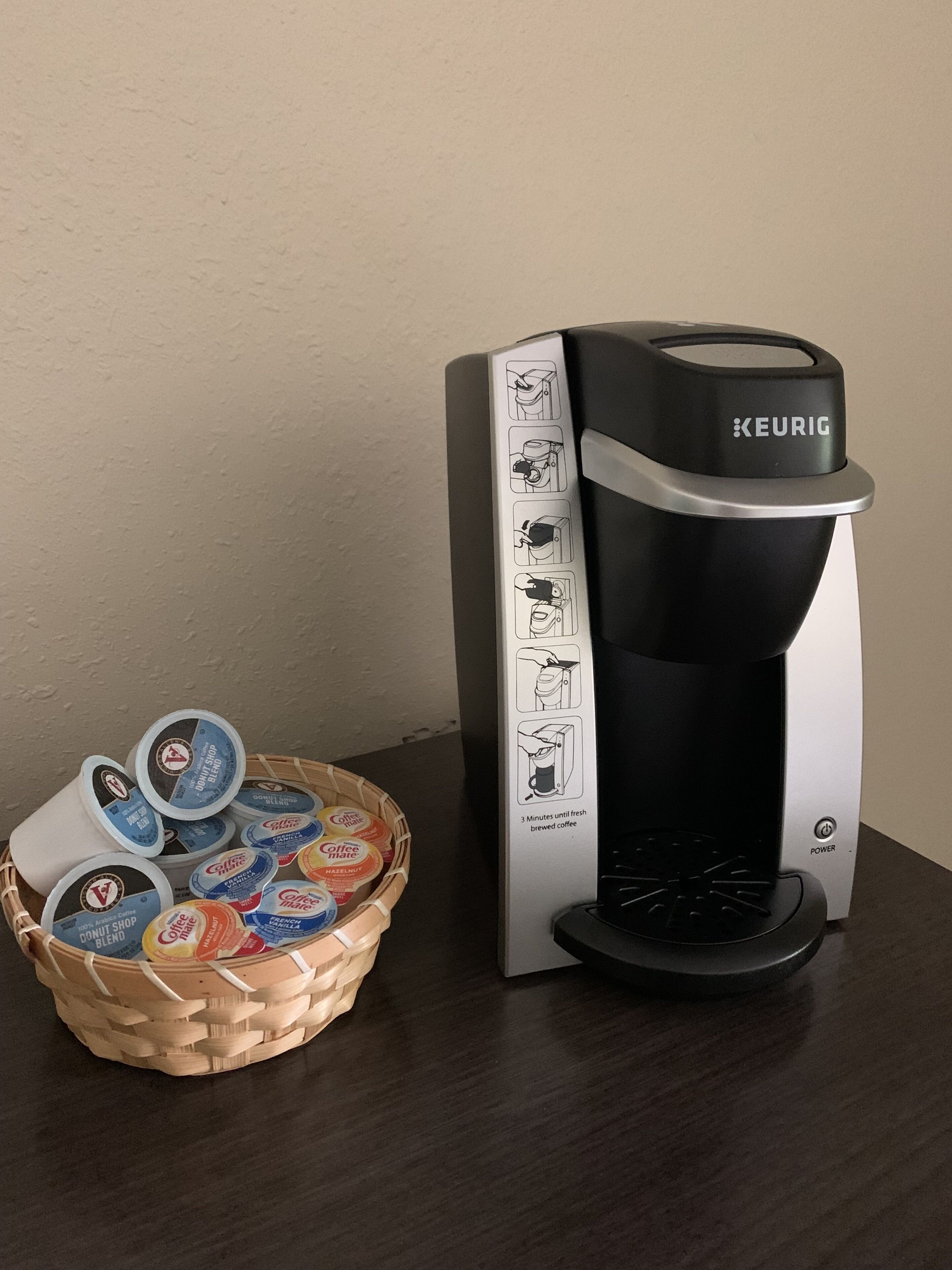 A Keurig coffee maker with a basket of coffee pods on a table.