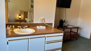A hotel bathroom with a sink, mirror, and a television mounted on the wall.